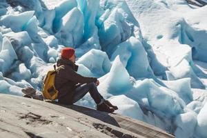 Reisender Mann sitzt auf einem Felsen auf dem Hintergrund eines Gletschers und Schnee foto
