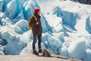 Reisender Mann, der auf einem Felsen auf dem Hintergrund eines Gletschers steht foto