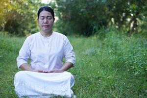 asiatisch Frau Buddhist trägt Weiß Kostüm, tun Meditation Sitzung beim still Wald. Konzept, Kultur von Glaube. religiös Aktivität. Frieden von Verstand Management. machen Konzentration. foto