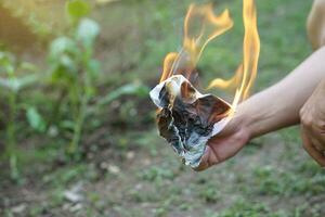 schließen oben Hand halt Feuer Verbrennung auf Papier. Konzept, zerstören dokumentieren, Geheimnis oder Beweise durch Feuer. Start Beleuchtung Feuer. leichtsinnig Feuersetzen ist gefährlich, Ursache Feuer Tragödie. foto