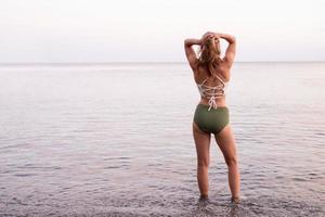 junge sportliche Frau steht am steinigen Strand mit Blick auf das Meer foto