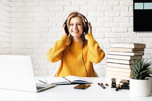 junge lächelnde Frau in schwarzen Kopfhörern, die online mit Laptop studiert?