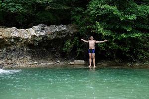 Mann schwimmt im Bergfluss mit Wasserfall foto