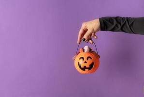 Halloween-Hand mit schwarzen Nägeln hält Kürbis voller Süßigkeiten foto