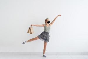junge Frau tanzt Ballett mit Einkaufstüten in einer Schutzmaske foto