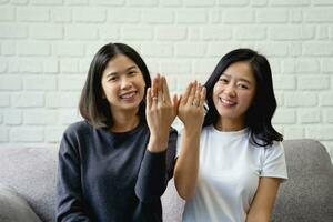 lächelnd asiatisch lgbtq Lesben Mädchen zeigt an aus ihr doppelt Hochzeit Ringe im Liebe und Glück zum lgbtq Stolz Monat. foto