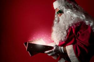 Santa claus Öffnung ein Geschenk Box voll von Weihnachten Magie Staub auf ein rot Hintergrund foto