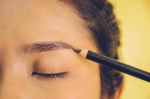 Schönheitsgesicht der asiatischen Frau durch Auftragen des Augenbrauenstiftes auf die Haut.
