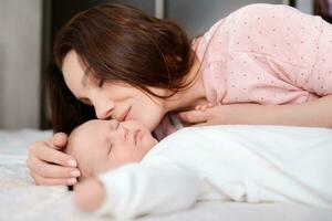 jung Frau liebevoll sieht aus beim ihr Schlafen Neugeborene Tochter im das Schlafzimmer foto