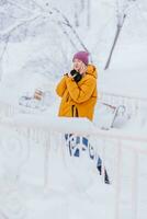 schön Mädchen im ein Gelb Jacke Fotograf nimmt Bilder von Schnee im ein Winter Park foto