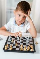 Clever Junge lernt zu abspielen Schach durch selbst im seine Zimmer beim Zuhause foto