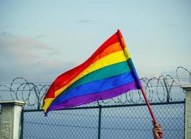 LGBTQ-Flagge mit einem Stacheldrahtzaun im Hintergrund.