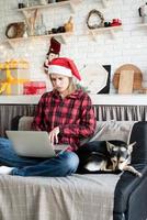 junge blonde Frau in Weihnachtsmütze arbeitet am Laptop foto