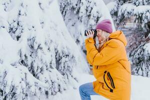 ein schön Mädchen mit ein Kamera im ihr Hände nimmt Bilder von Winter im ein schneebedeckt Park foto