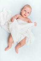 Porträt von ein schön Baby Mädchen Lügen auf ein Weiß Blatt im ihr Zimmer foto