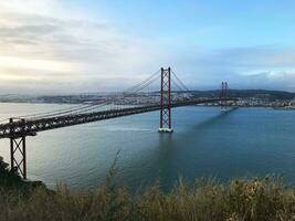 das ikonisch Brücke über das Blau Wasser von das Tagus von Almada zu das überfüllt Ufer von Lissabon, Portugal beschwingt Hauptstadt Stadt. foto