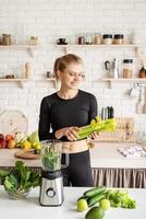 junge blonde lächelnde Frau macht Sellerie-Smoothie zu Hause in der Küche foto