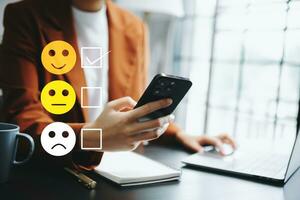 Kundenservice-Bewertungskonzept. frau zeigt gesicht lächeln emoticon zeigen auf virtuellem bildschirm von hand. blick auf smartphone, tablet und laptop foto