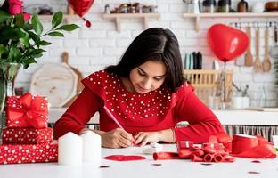 Frau schreibt Liebesbrief sitzend in der dekorierten Küche foto