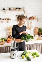 junge blonde lächelnde Frau macht Spinat-Smoothie zu Hause Küche foto