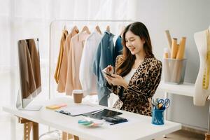 asiatisch Schneider Frau Arbeiten auf Kleider im Schneiderei Atelier. schön jung weiblich Mode Designer Lächeln und nach Erfolg im modern tudi foto