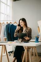 asiatisch Schneider Frau Arbeiten auf Kleider im Schneiderei Atelier. schön jung weiblich Mode Designer Lächeln und nach Erfolg im modern tudi foto