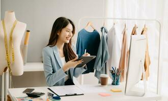 asiatisch Schneider Frau Arbeiten auf Kleider im Schneiderei Atelier. schön jung weiblich Mode Designer Lächeln und nach Erfolg im modern tudi foto