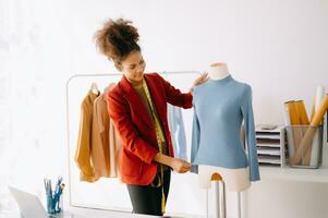 afrikanisch Schneider Frau Arbeiten auf Kleider im Schneiderei Atelier. schön jung weiblich Mode Designer Lächeln und nach Erfolg im Studio foto