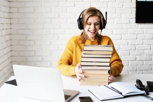 Frau mit schwarzen Kopfhörern, die online studiert und einen Stapel Bücher hält