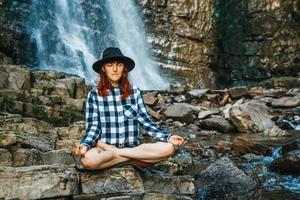 Frau mit Hut und Hemd, die auf Felsen im Lotussitz meditiert foto