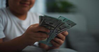 Porträt schließen oben Hände von jung asiatisch Frau genießen Zählen Kasse Dollar Banknoten auf Sofa im das Leben Zimmer beim heim. foto