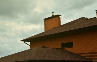 Das Haus ist mit einer hochwertigen Dacheindeckung aus Schindeln aus Bitumenziegeln ausgestattet. ein gutes Beispiel für eine perfekte Überdachung. Das Dach ist zuverlässig vor Witterungseinflüssen geschützt foto