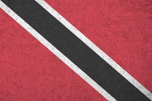 die flagge von trinidad und tobago ist in hellen farben auf einer alten reliefputzwand dargestellt. strukturierte Fahne auf rauem Hintergrund foto