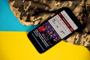Kiew, Ukraine - - 4 dürfen, 2023 oben ukrainska Prawda ukrainisch Nachrichten Portal auf Smartphone Bildschirm mit ukrainisch Flagge und tarnen Stoff foto