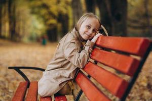 ein kleines mädchen in einem gelben kleid und beige mantel spaziert im herbstpark foto