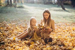 Mutter und ihre Tochter sitzen und haben Spaß im Herbstpark. foto