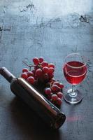 Rotwein und Weinflasche mit Trauben auf schwarzem Hintergrund foto