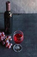 Rotwein und Weinflasche mit Trauben auf schwarzem Hintergrund foto