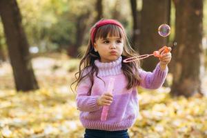 kleines Mädchen, das mit Seifenblasen von Herbstblättern im Park spielt foto