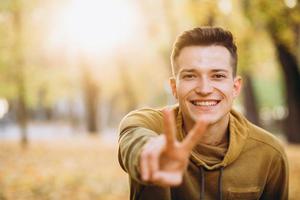 Kerl, der im Herbstpark lächelt und Frieden zeigt foto