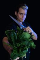 veganer Koch hält ein Bündel rohen Spinat und Messer foto