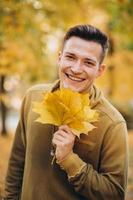 Kerl lächelt und hält einen Strauß Herbstblätter im Park