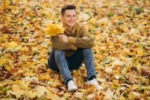 Junge mit einem Blätterstrauß, der im Herbstpark lächelt und träumt foto