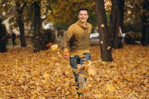 gut aussehender Kerl lächelt und rennt verstreute gelbe Blätter im Herbstpark foto
