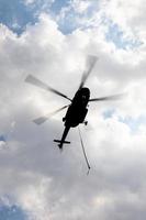 Silhouette fliegender Hubschrauber mit Schlinge bei bedecktem Himmel. foto