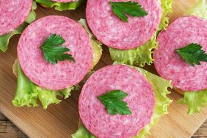 Sandwiches mit Salatblättern und geschnittener Salamiwurst auf einem Holzbrett. foto