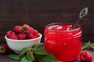 hausgemachte Himbeermarmelade in einem Glasgefäß und frische Himbeeren mit Minze auf einem hölzernen rustikalen Hintergrund. Platz kopieren foto