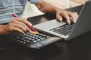 Hand, die einen Bleistift, einen Taschenrechner und eine Computertastatur auf dem Schreibtisch hält. foto