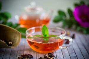 gebraut Hagebutte Tee im ein Glas Teekanne mit Hagebutte Blumen und Minze foto