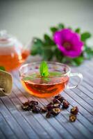 gebraut Hagebutte Tee im ein Glas Teekanne mit Hagebutte Blumen und Minze foto